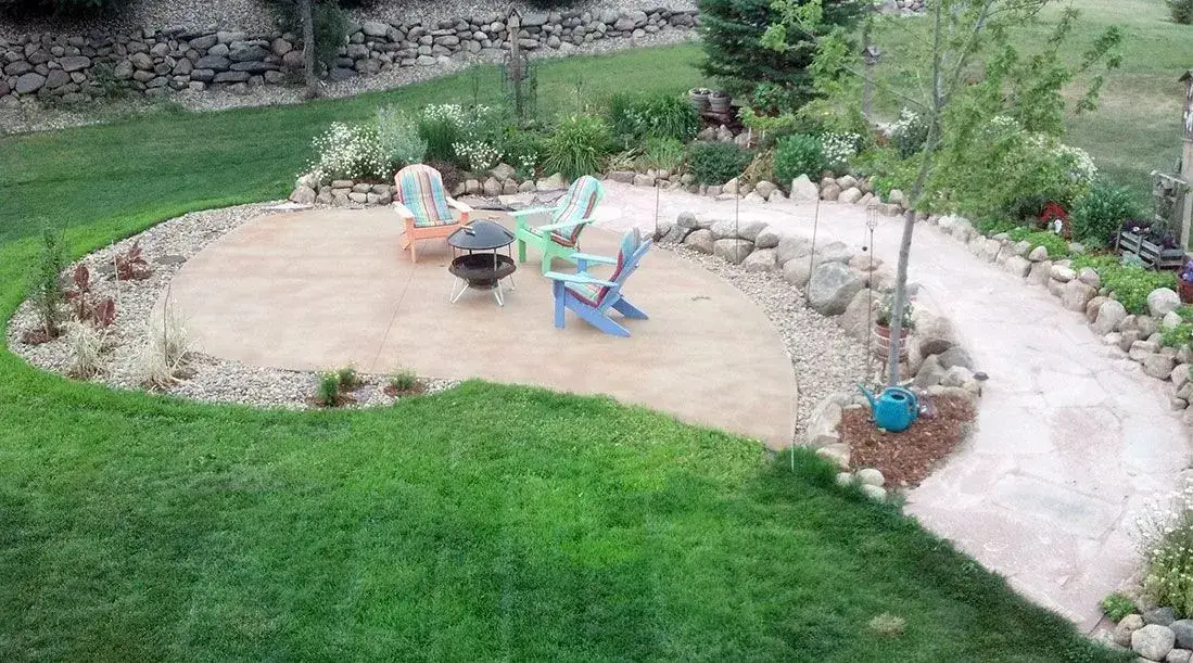 Round tan colored concrete patio with fire pit in a landscaped backyard